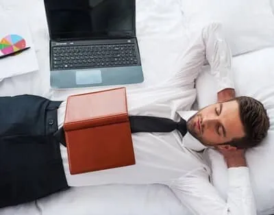 homme affaire en costume allonge dans un lit hotel avec ordinateur Homme d’affaires en costume qui se détend sur le lit d'une chambre d'hôtel avec son ordinateur portable et un dossier, idéal pour une soirée étape solo.